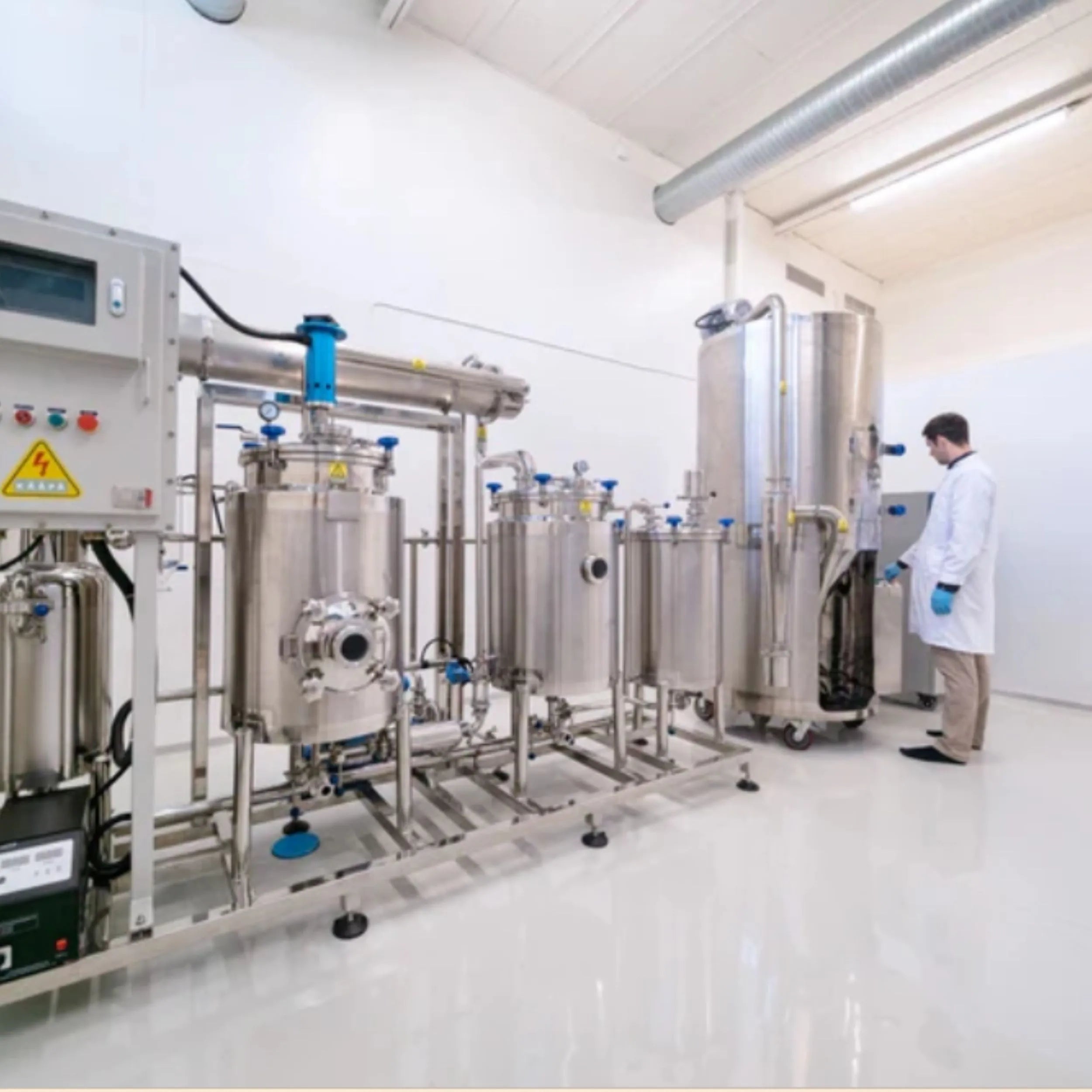Moderner Produktionsraum mit großen Edelstahlbehältern zur Extraktion von Vitalpilzen, ein Laborant im weißen Kittel bedient die Anlage – hygienische Herstellungsumgebung bei KÄÄPÄ Mushrooms.