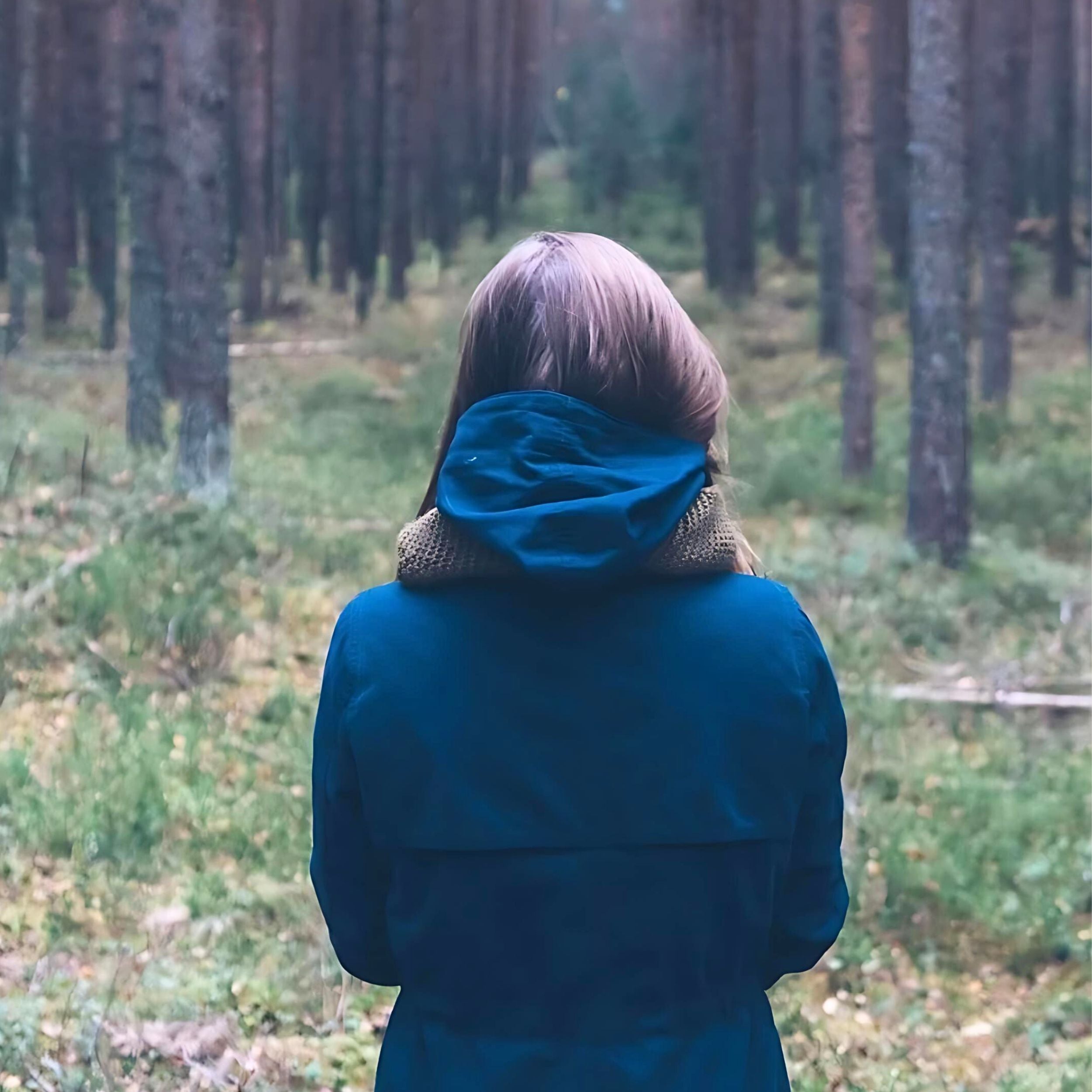 Rückansicht einer Person im blauen Mantel, die in einem dichten, ruhigen Wald steht – Symbol für Naturverbundenheit und Achtsamkeit.